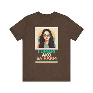 Può includere: Una t-shirt marrone con un'illustrazione in stile retrò di una donna con occhiali da sole. Il testo "Lumaki Ako Sa Farm" è stampato sotto l'immagine.