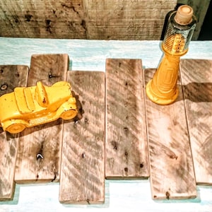May include: A yellow toy car and a yellow bottle with a cork top are displayed on a rustic wooden surface. The car has a vintage design. The bottle has a measuring scale inside. The background is a light blue painted wood.