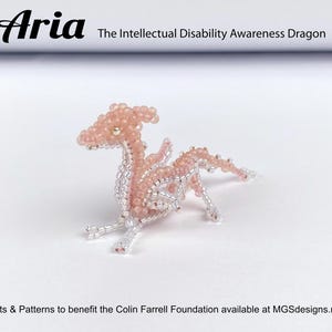 Könnte beinhalten: Eine rosa Perlen-Drachenfigur, bekannt als "Aria", der Drache für das Bewusstsein für geistige Behinderung. Der Drache ist in einer Pose mit ausgebreiteten Flügeln und geneigtem Kopf dargestellt.