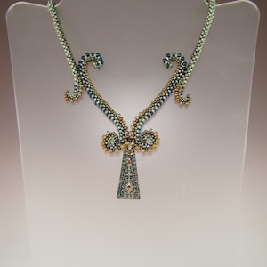 May include: A green, blue, and gold beaded necklace with a decorative pendant. The pendant is a triangular shape with a geometric pattern.