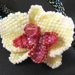 May include: A white and pink beaded orchid flower pendant with a crystal center.