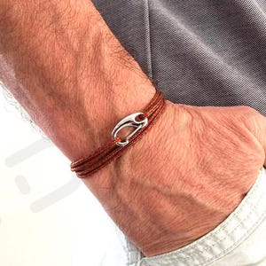 Könnte beinhalten: Ein braunes Lederarmband mit einem silbernen Verschluss. Das Armband wird am Handgelenk getragen.