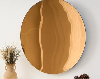 May include: A large, round, bronze-colored mirror with a black frame. The mirror reflects the light, creating a wavy pattern on its surface. The mirror is a decorative item, suitable for any room.