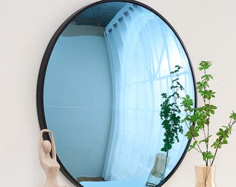 May include: A round blue mirror with a black frame. The mirror is reflecting a white curtain and a plant in a vase.