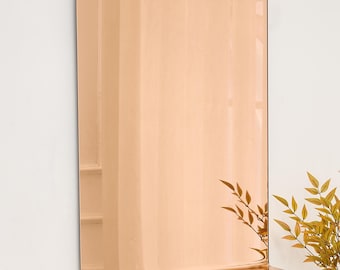 May include: A rectangular, rose-gold mirror with a built-in shelf. The mirror has a sleek, modern design with rounded corners and a reflective surface. The shelf is a simple, horizontal plane, perfect for displaying small items. The mirror is mounted on a white wall.