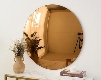 May include: A large circular wall mirror with a warm bronze-tinted reflective surface. The mirror reflects a room interior, including a tripod and curtains. It is positioned above a white marble-topped console table with a gold metal frame.