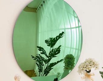 May include: A round green mirror with a slightly distorted reflection of a plant and a white curtain. The mirror is hanging on a white wall.