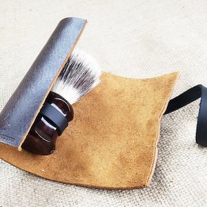 May include: A brown leather shaving brush holder with a black leather strap. The holder is rolled up and has a shaving brush inside.
