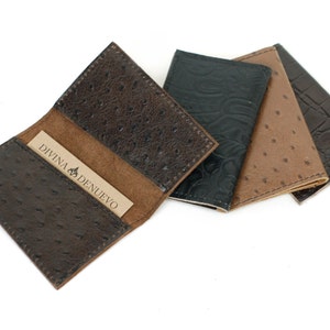May include: Three leather card holders in brown, black, and dark brown with an ostrich skin pattern. The brown card holder has a business card inside that reads "Divina Denuevo".