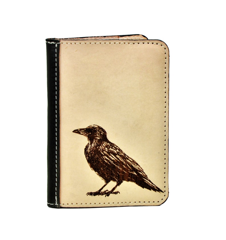 May include: A beige leather wallet with a black stitched border and a brown crow design.