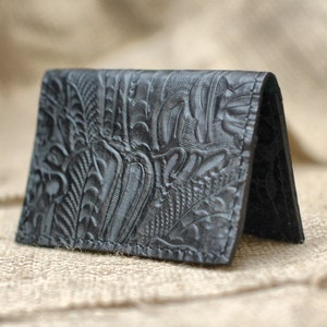May include: A black leather card holder with an embossed floral pattern.