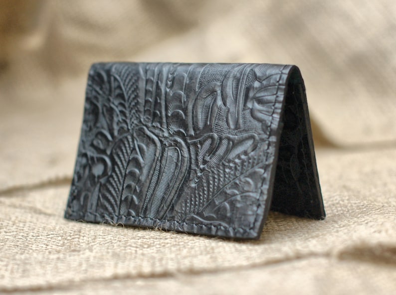 May include: A black leather card holder with an embossed floral pattern.