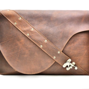May include: A brown leather messenger bag with a flap closure and a silver buckle. The bag has a long adjustable strap with silver studs.