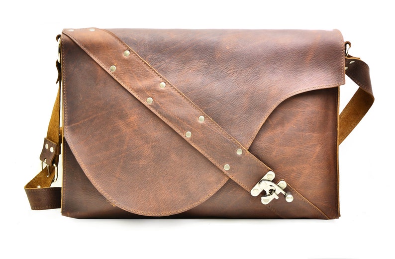 May include: A brown leather messenger bag with a flap closure and a silver buckle. The bag has a long adjustable strap with silver studs.