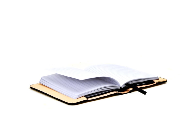 May include: A brown leather bound journal with a black ribbon bookmark. The journal is open to a blank page with lined paper.