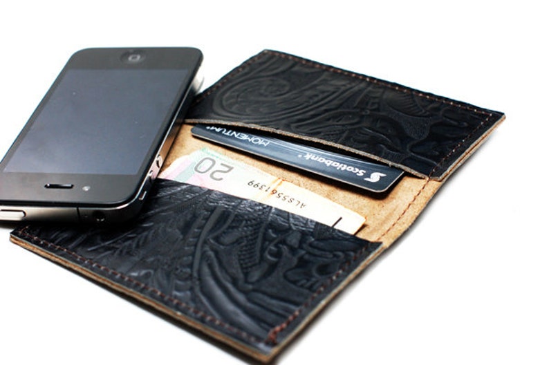 May include: A black leather wallet with an embossed design. The wallet is open and shows a credit card, cash, and a smartphone.