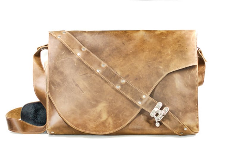 May include: A brown leather messenger bag with a silver buckle and a strap with silver studs.