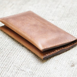 May include: A brown leather wallet folded closed. The wallet has a stitched edge and is made of a soft, supple leather.