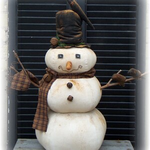 Puede incluir: Decoración de muñeco de nieve artesanal con sombrero de copa negro, bufanda y brazos de ramitas. El muñeco de nieve tiene una nariz de zanahoria, ojos de botón y una bufanda a cuadros. Se adjuntan campanas decorativas al sombrero y la bufanda.