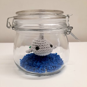 May include: A crocheted gray whale figurine inside a clear glass jar filled with blue plastic pellets.