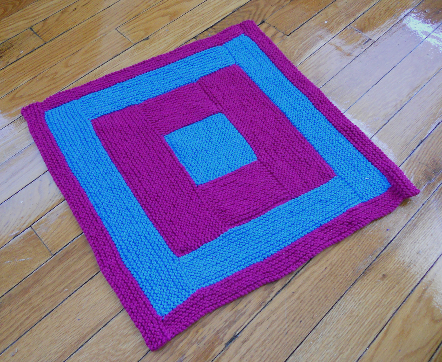 May include: A square knitted throw blanket with a concentric square pattern in pink and blue.