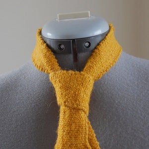 May include: A yellow knitted scarf tied in a knot around a mannequin's neck.