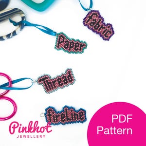 May include: Four beaded word charms with the words "Fabric", "Paper", "Thread", and "Fireline". The charms are pink with black lettering and have blue and green beads around the edges. The charms are hanging from blue ribbon.