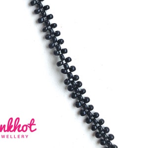 May include: A close-up of a black zipper chain, made of small, round beads. The chain is on a white background.