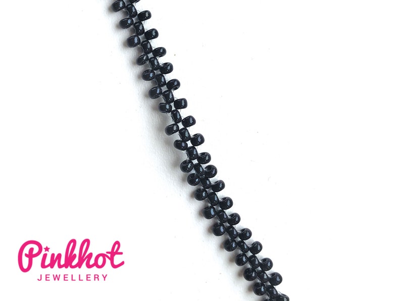 May include: A close-up of a black zipper chain, made of small, round beads. The chain is on a white background.