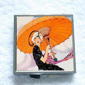 May include: A vintage illustration of a woman in a black dress holding an orange parasol. The woman is wearing a white turban and has a blue jewel in her ear. The parasol is open and has a woven handle.