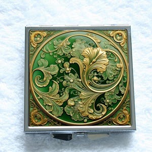 May include: A square metal compact with a hinged lid. The lid features a green and gold design with intricate floral patterns.