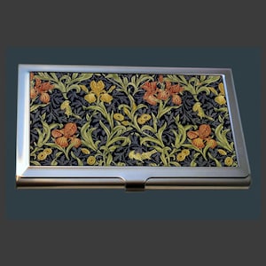 May include: A silver business card holder with a floral pattern. The design includes orange and yellow irises, green leaves, and small yellow birds on a dark blue backdrop. The holder is rectangular.