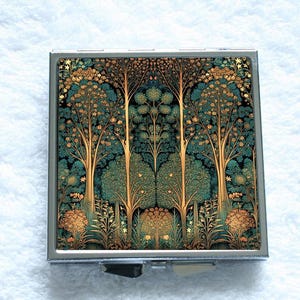 Peut inclure: Un miroir de poche argenté avec une scène de forêt détaillée. Le motif présente des arbres stylisés avec des troncs dorés et un feuillage vert-bleu sur fond noir. Le compact est carré et s'ouvre avec une charnière.