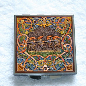 May include: A square metal compact case featuring a relief carving of four gnomes in red hats running in a line. The design is surrounded by intricate, colourful Celtic-style knotwork in shades of orange, blue, green, and yellow on a dark background.