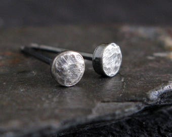 May include: A pair of silver-toned stud earrings featuring small, circular faces with a textured, hammered finish. Each earring has a thin metal post extending from the back of the round head, designed for insertion through a pierced earlobe.