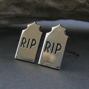 May include: A pair of silver earrings shaped like tombstones with the word "RIP" engraved on each.