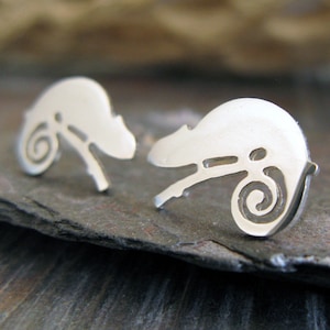 May include: A pair of silver chameleon earrings. The earrings are made of a thin metal and are shaped like a chameleon. The chameleon is curled up in a spiral shape.