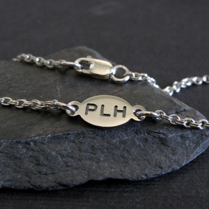 以下が含まれることがあります： PLH と刻まれた楕円形のチャームが付いたシルバーチェーンブレスレットです。