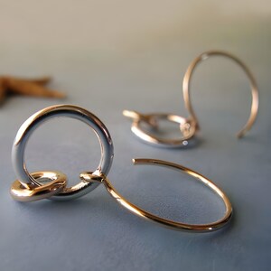 Pode incluir: Um par de brincos de argola de prata e ouro com um design de nó. Os brincos são simples e elegantes.