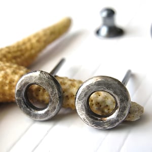 May include: A pair of silver circle stud earrings with a hammered texture. The earrings have a simple, minimalist design.