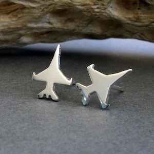 May include: A pair of silver airplane stud earrings. The earrings are made of polished silver and are shaped like airplanes. The airplanes are facing different directions.