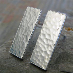 Op de afbeelding: Een paar zilveren gehammerde rechthoekige oorbel studs. De oorbellen zijn gemaakt van sterling zilver en hebben een textuur.