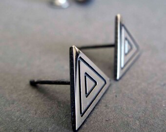 May include: A pair of silver triangle stud earrings with a geometric design. The earrings are made of metal and have a polished finish.