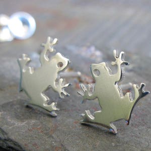 May include: A pair of silver frog stud earrings. The frogs are facing to the right and have a detailed silhouette design.