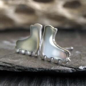 May include: A pair of silver boot earrings. The boots are detailed with a textured sole and a rounded toe.