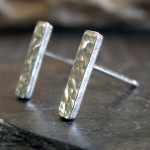 May include: A pair of silver stud earrings with a hammered texture. The earrings are rectangular in shape and have a subtle shine.