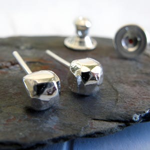 May include: A pair of silver earrings with a hammered, faceted, geometric design. The earrings are small and have a post back.
