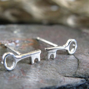 Könnte beinhalten: Ein Paar silberne Schlüssel-Ohrstecker. Die Ohrringe sind klein und zart und wären ein tolles Geschenk für jemanden, der Schlüssel oder Vintage-Schmuck liebt.