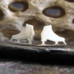 May include: A pair of silver ice skate earrings. The earrings are shaped like ice skates and have a shiny finish.