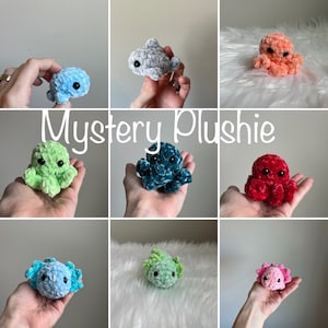 May include: A collection of handmade crocheted plush toys in various colors, including green, blue, red, and pink. The toys are shaped like octopuses and are displayed on a white background. The text "Mystery Plushie" is displayed in the center of the image.